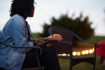 a woman sitting in a chair with a hotdog on her plate at an outdoor party 