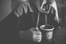 A boy sits at a table with a cup of cocoa.
