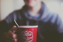 Someone holds a red coffee cup with a scripture written on it.