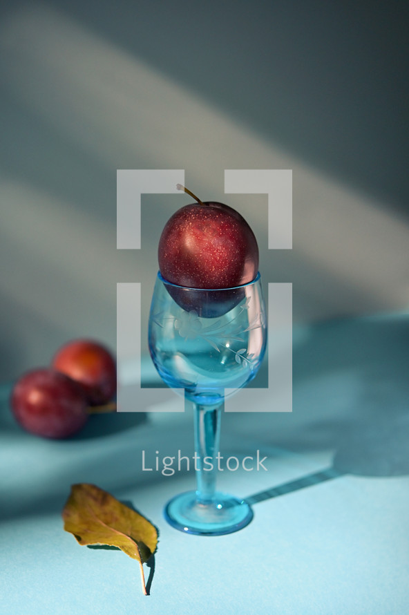A plum in a turquoise glass cup with fall leaf on the table