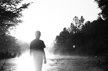 a young man standing by a river under intense sunlight 