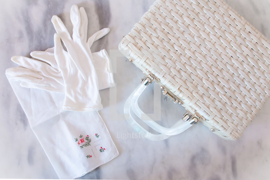 White gloves, handkerchief, and straw handbag on a marble table