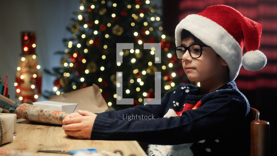 Kid preparing Christmas gifts for his friends on table