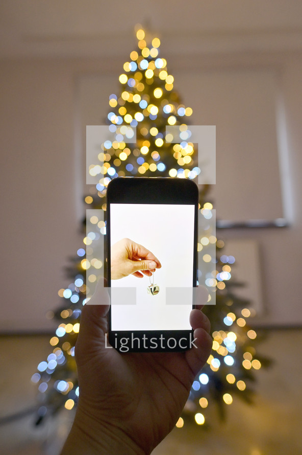 Image of a hand holding a bell on a phone in front of a Christmas tree