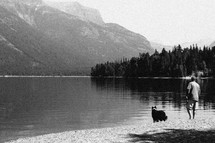 a man and his dog walking around a mountain lake shore 