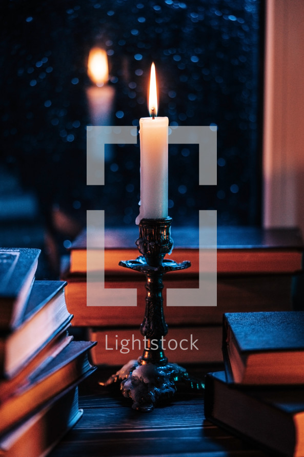 Stack of old paper books on wooden windowsill, bathed in soft candle glow light. Cozy ambience of fall, candle burning. Literature promotions or tranquil visual storytelling. Rainy autumn weather.