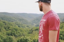 man in a ball cap looking out at mountains 
