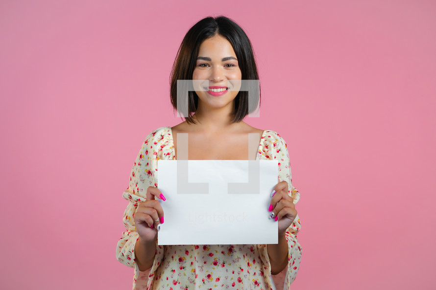 Portrait of young woman holding white horizontal a4 paper isolated on pink studio background. Copy space. High quality photo