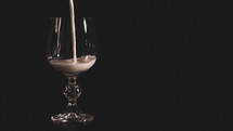 A transparent glass for wine is filled with milk on a black background
