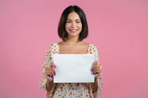 Portrait of young woman holding white horizontal a4 paper isolated on pink studio background. Copy space. High quality photo