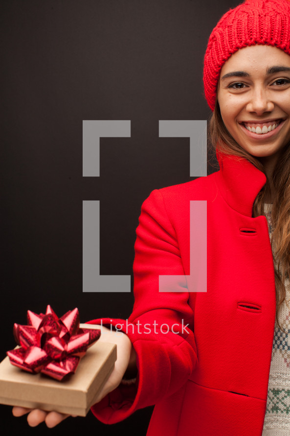a woman in a red trench coat holding a gift box 