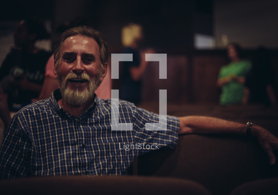 A bearded man sitting in a church auditorium.