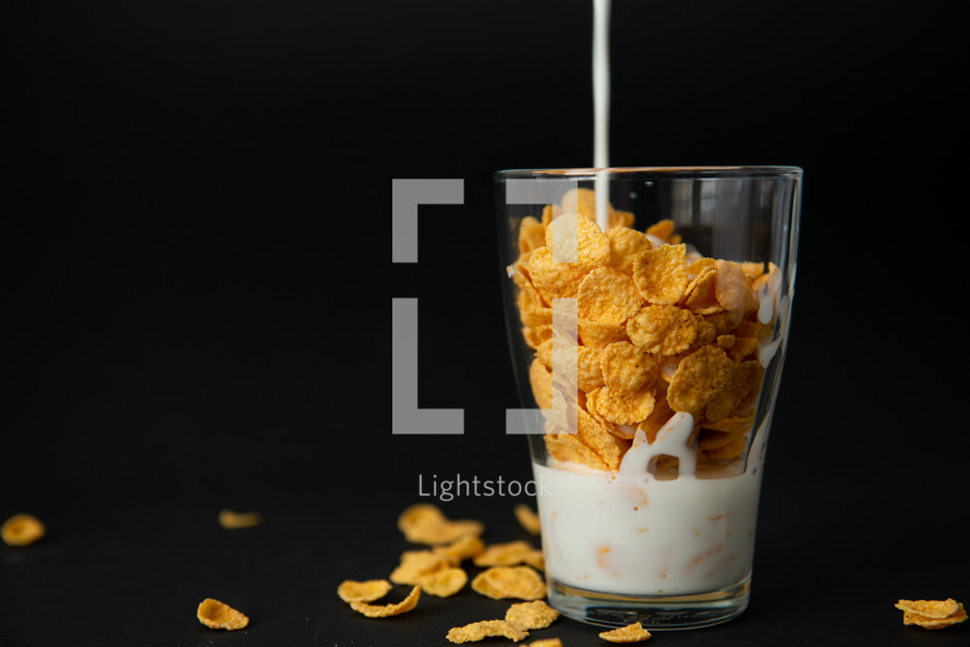 cornflakes with milk in a transparent glass against a black background with place for text