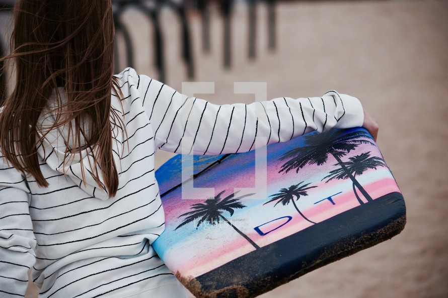 a girl carrying a boogie board on a beach 