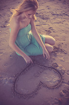 A woman drawing a heart in the sand.