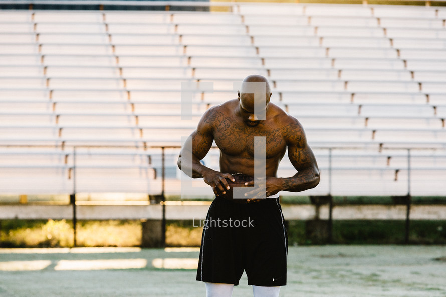 a shirtless man with tattoos standing on a football field 