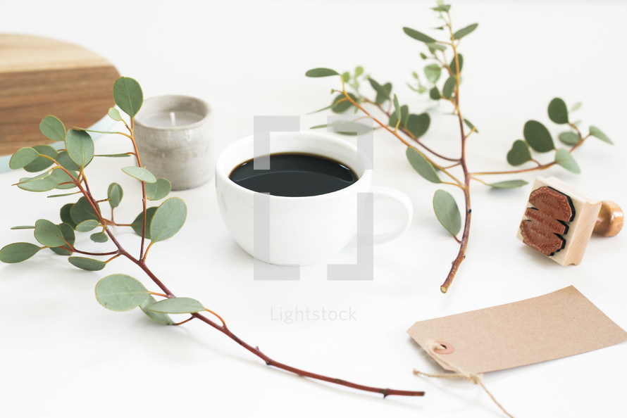 candle, coffee cup, eucalyptus twigs, gift tag, stamp, on a white table 