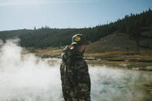 steam rising from a lake and man in a camouflage coat 
