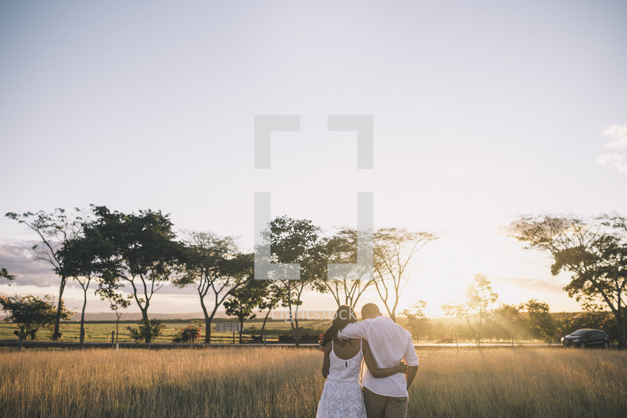 husband and wife walking through tall grass at sunset 