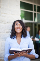 a smiling woman holding a Bible looking up to God 
