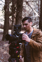 man standing in a forest with a video camera 
