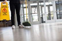 a man with a dust mop and wet floor sign in a lobby