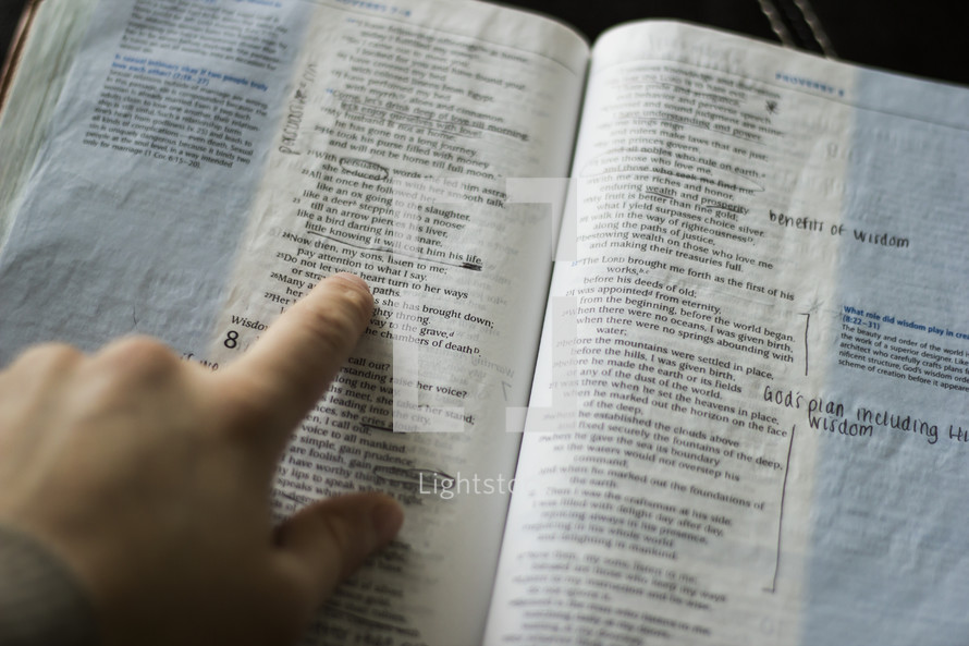 A hand pointing to a verse in a Bible.