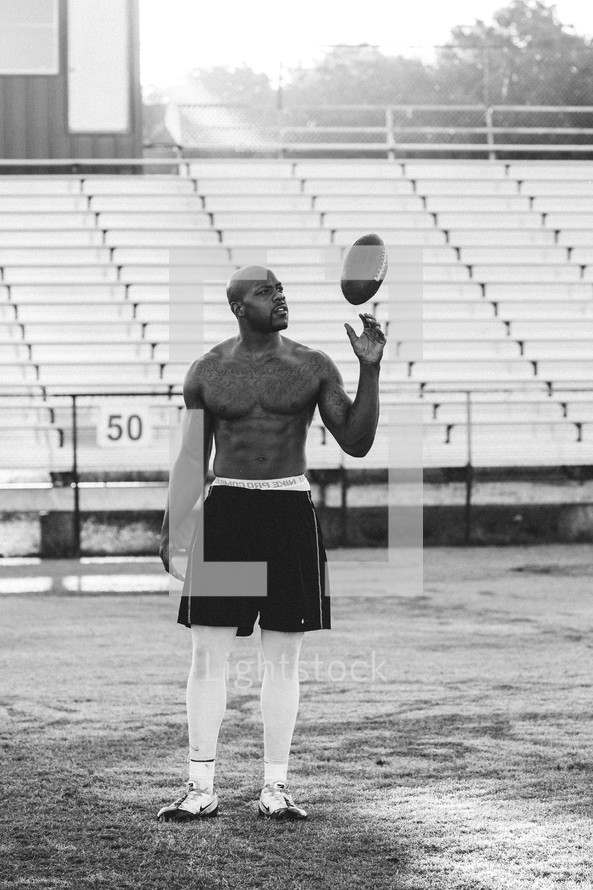 a shirtless man with tattoos holding a football on a field 