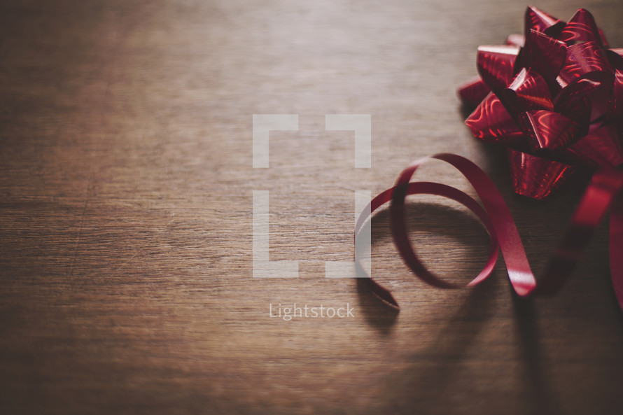 a shiny red bow and ribbon on wood