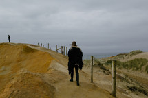 A woman walking along a sand dune near the ocean.