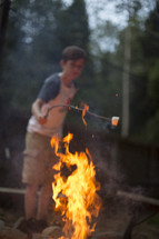 A boy roasting a marshmallow over a campfire.