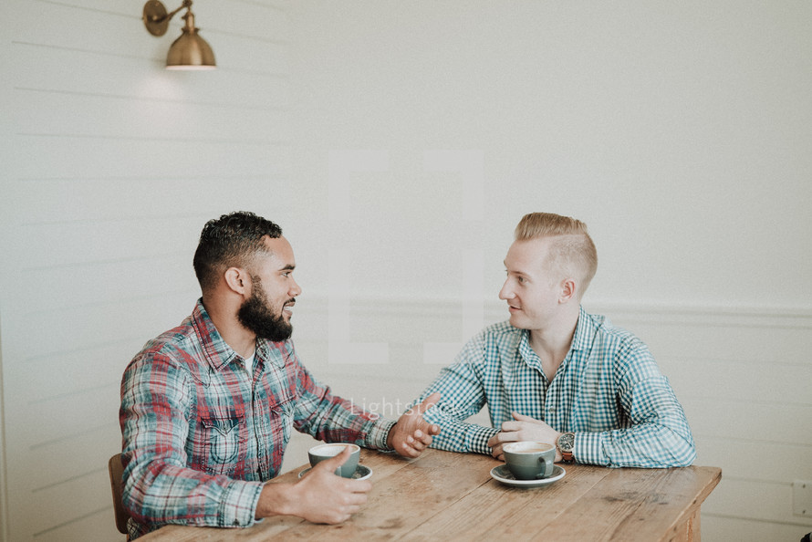 two men talking while sitting at a table drinking coffee 
