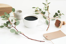 candle, coffee cup, eucalyptus twigs, gift tag, stamp, on a white table 