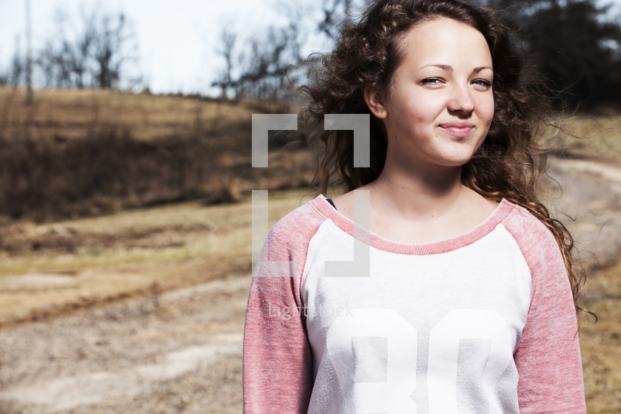 Smiling girl standing outside by a dirt road.