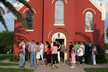 congregation gathered in front of a red church 