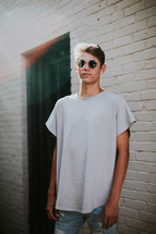 teen boy standing in front of a white brick wall in sunglasses 