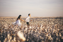 a couple holding hands running through a field of cotton 