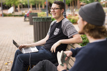 college students sitting on a park bench with a laptop and books studying 