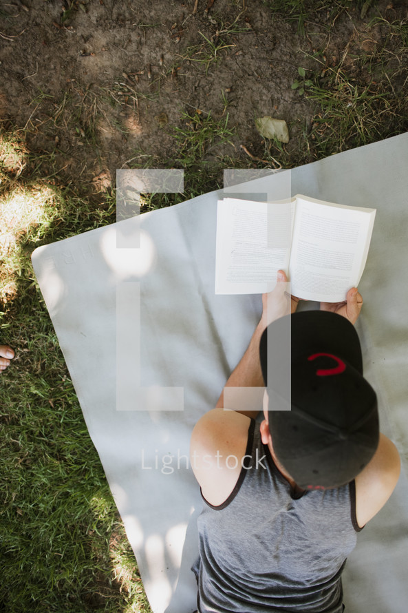 man reading a book lying on a blanket in the grass