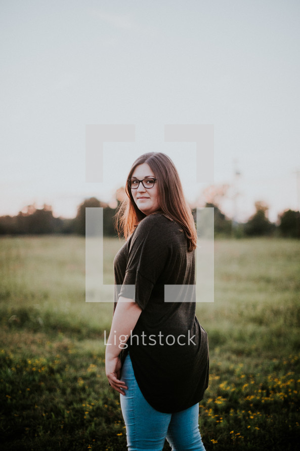 a woman standing in a field at sunset 