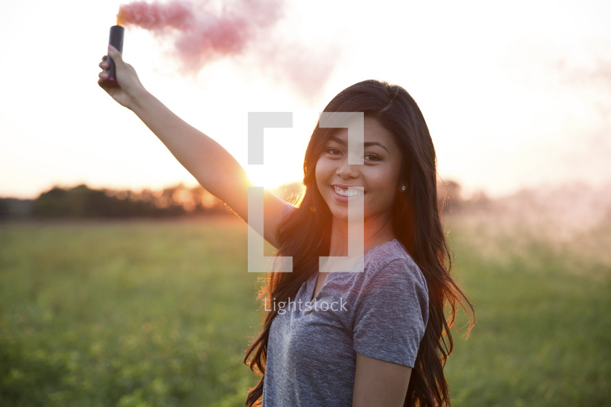 young woman holding a smoke flare at sunset 