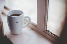 A cup of tea sits on a windowsill.