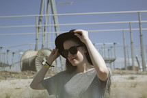 a woman standing outdoors wearing a hat and sunglasses 