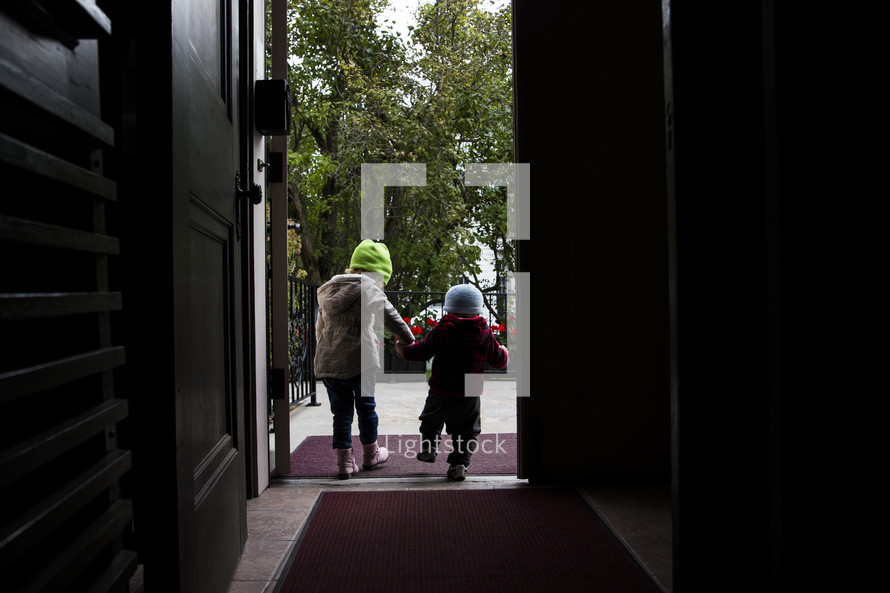 siblings holding hands walking through a doorway 