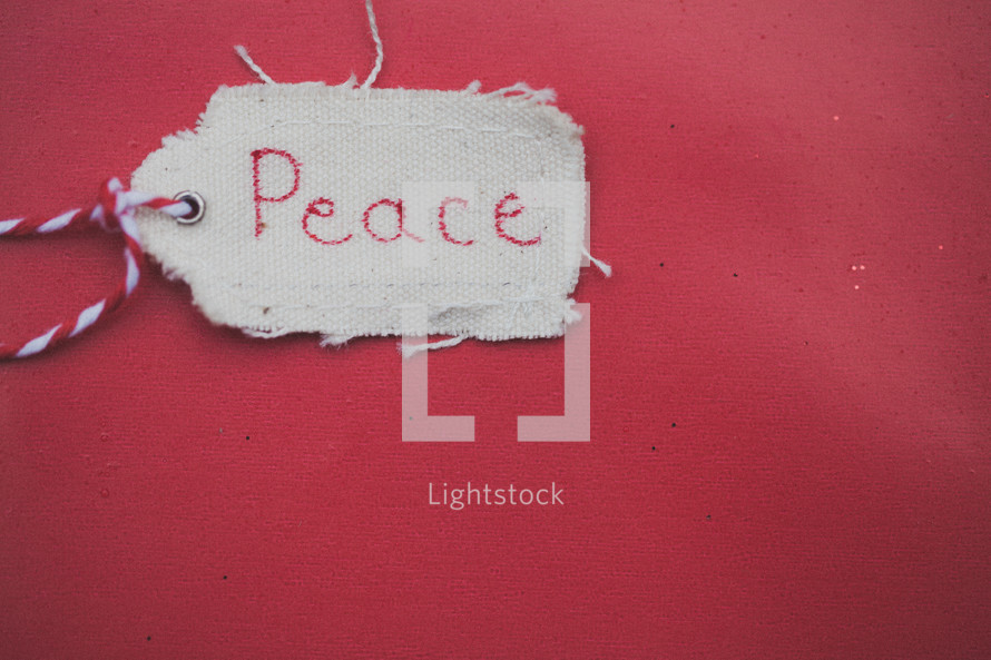 A Christmas gift tag reading "Peace," on a red background.