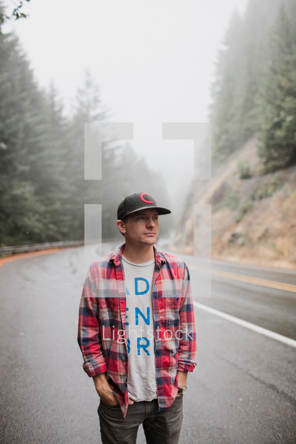 man in a ball cap and plaid shirt standing on the side of a road 