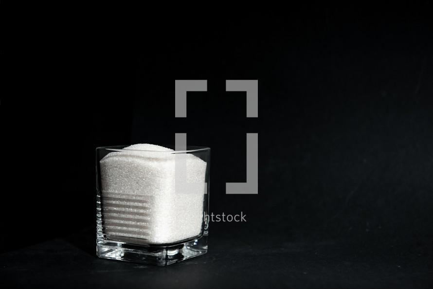 sugar in a transparent glass with a corrugated face on a black background