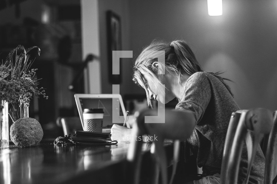 a woman sitting at a table working and writing with a laptop and coffee cup 