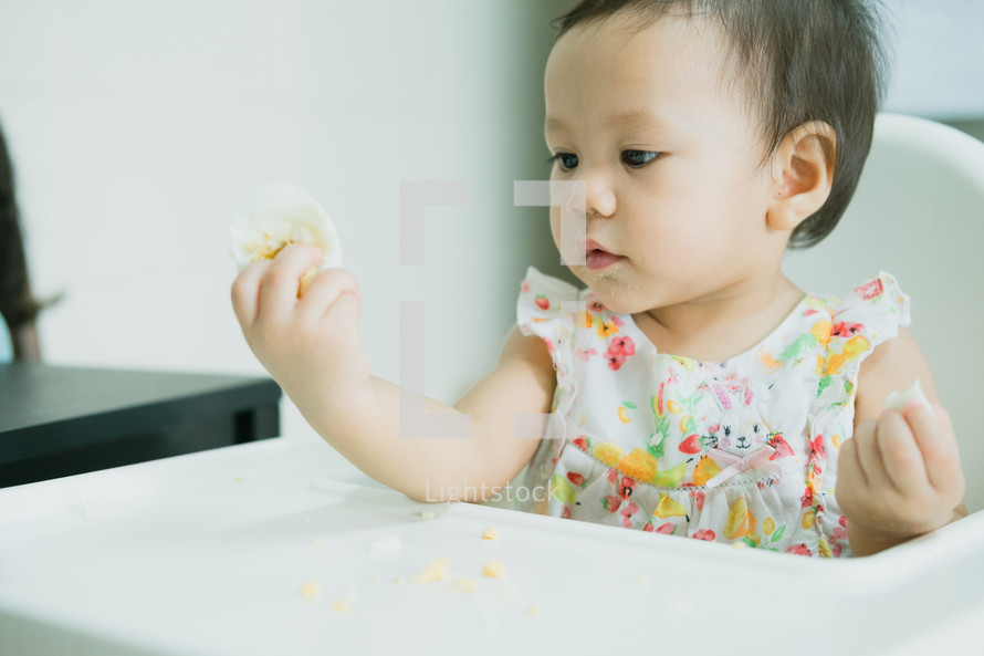toddler girl eating in a highchair 