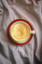 Flat lay of a cup of cappuccino coffee in bed on crumpled sheets